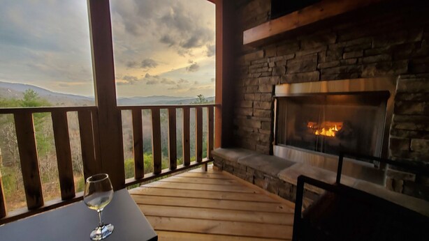 A wooden deck with a stone fireplace and a glass of wine on a table. - "Her Endless Views" cabin has incredible mountain views, hot tub, and firepit (Murphy)