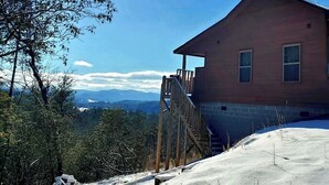 A house with a wooden staircase leading up to a porch, surrounded by snow and trees. - "Her Endless Views" cabin has incredible mountain views, hot tub, and firepit (Murphy)