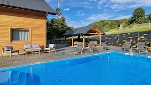 A wooden building with a pool, lounge chairs, and a covered area with a view of a landscaped hill. - Holiday Home Wisniowa With Pool and Mountains (gmina Iwierzyce)