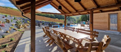 A covered outdoor seating area with wooden benches and a pool in the background.