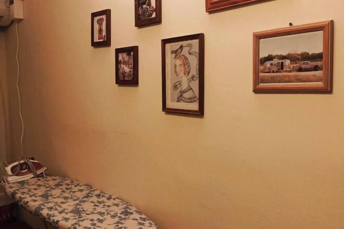 A room with a bed, a wall-mounted heater, and framed artwork.