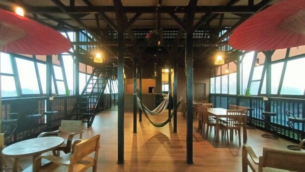 A spacious indoor area with wooden tables and chairs, a hammock, and large windows offering views. - Anggun Lodge Private Room with Sharing Bathroom (Semporna)