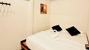 A neatly made bed with a white duvet, two black pillows, and a white towel. There is a small painting on the wall above the bed. - Anggun Lodge Private Room with Sharing Bathroom (Semporna)
