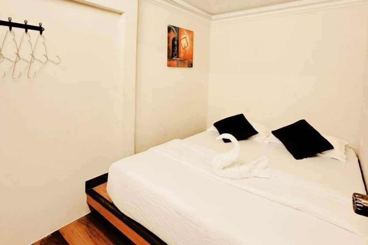 A neatly made bed with a white duvet, two black pillows, and a white towel. There is a small painting on the wall above the bed.