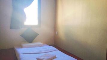 A small, simple room with a single bed, a pillow, and a window with curtains.