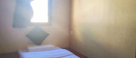 Una habitación pequeña y sencilla con una cama individual, una almohada y un ventanal con cortinas.