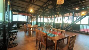 An indoor dining area with wooden tables and chairs, large windows, and a staircase.