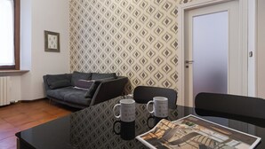 Une pièce avec un papier peint à motifs, un canapé gris, une table en verre avec deux tasses et une porte.