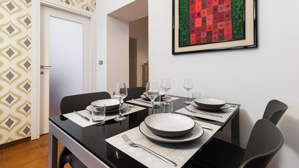 Une table à manger dressée avec des assiettes, des verres et des couverts, et une œuvre d’art encadrée accrochée au-dessus.