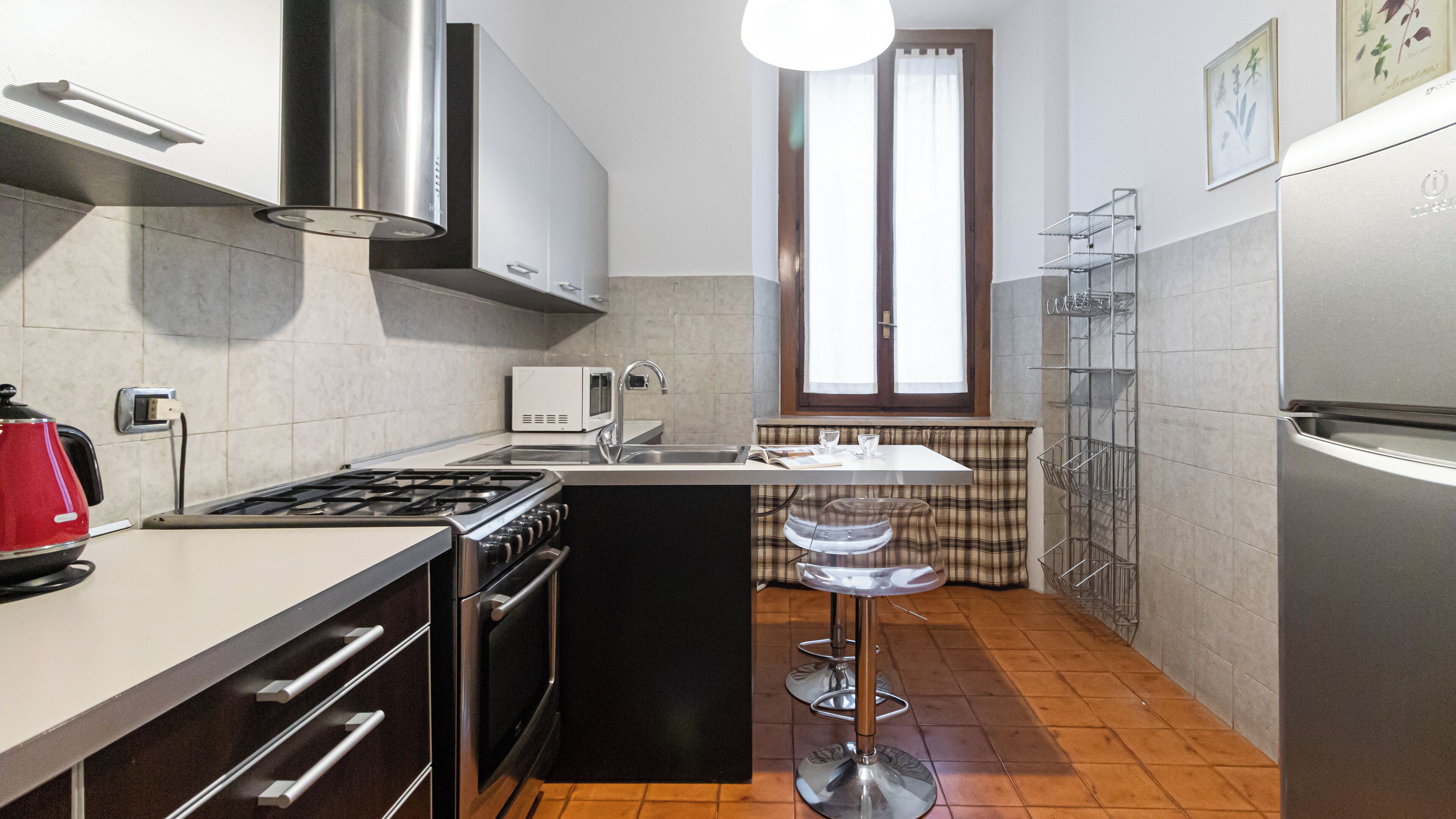 A compact kitchen with a stove, microwave, sink, and a small window.