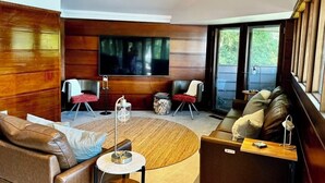 A modern living room with wooden paneling, a large flat-screen TV, leather sofas, and a round coffee table. - Stunning Waterfront Home with Private Dock - Wright on the Water! (Belle Haven)