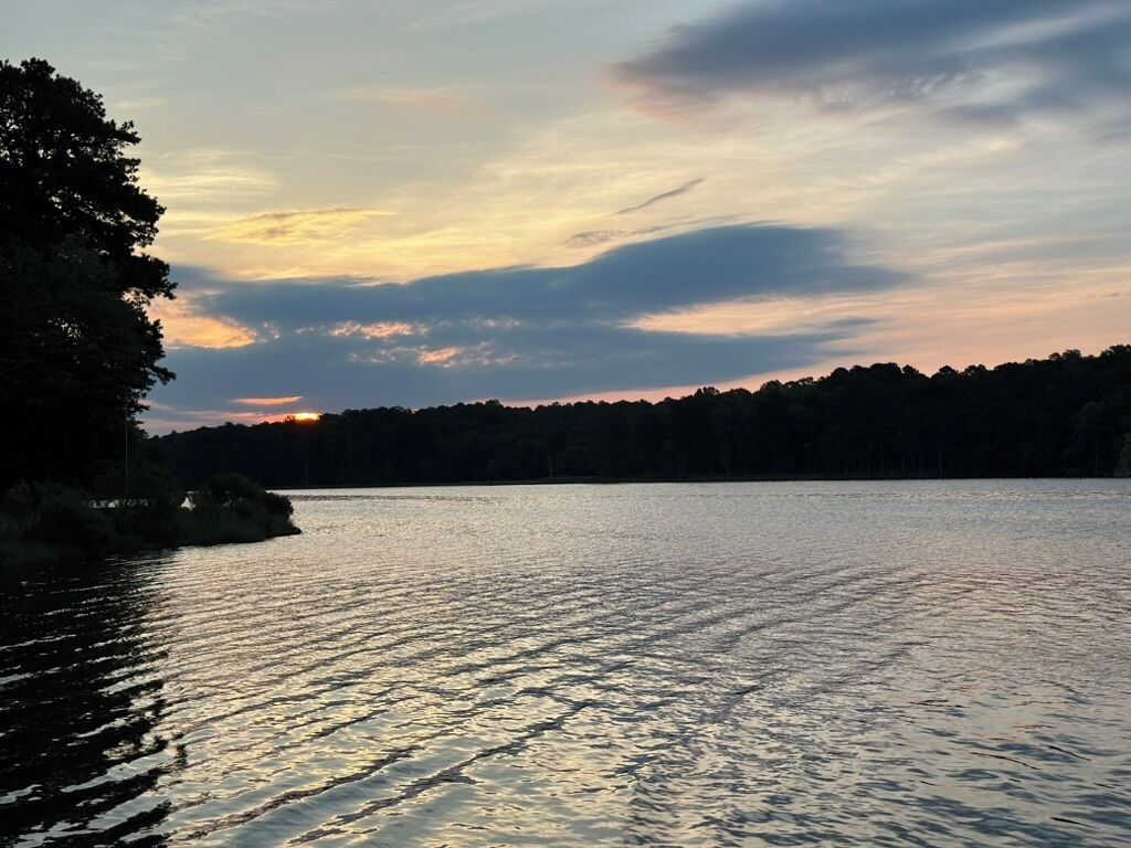 En stilla sjö vid solnedgången, med en skogbeklädd strand.