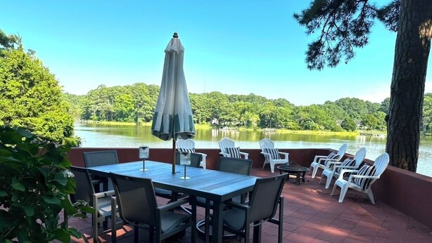 An outdoor patio with a table and chairs, overlooking a lake and forested area. - Stunning Waterfront Home with Private Dock - Wright on the Water! (Belle Haven)