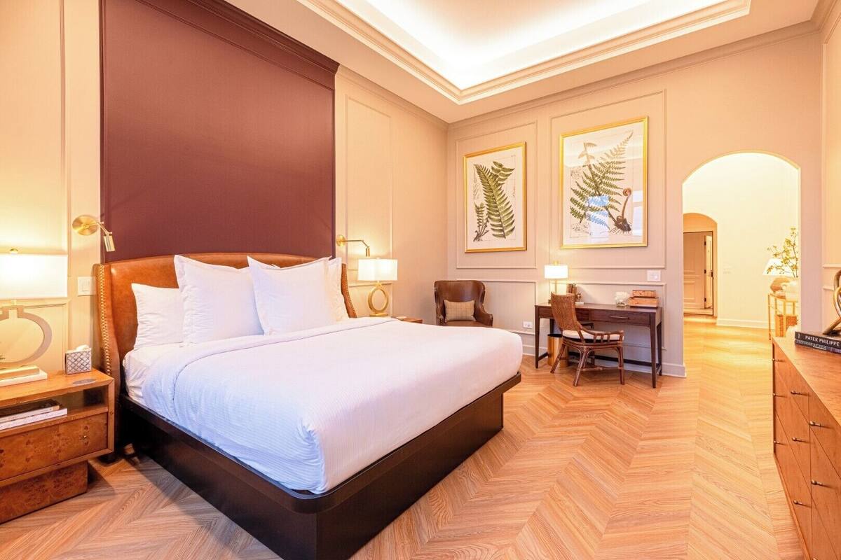 Une chambre d’hôtel avec un grand lit, un bureau, deux chaises et des reproductions encadrées de motifs botaniques accrochées au mur.