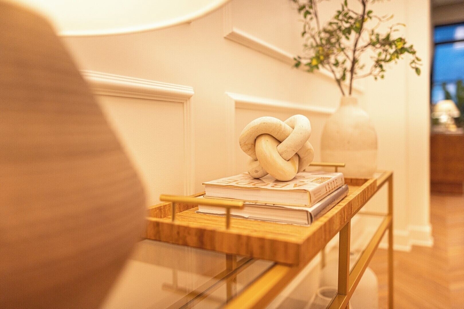 Een houten bijzettafeltje met een glazen blad, een boek en een decoratieve knoopsculptuur.