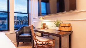 Une chambre d’hôtel équipée d’un bureau, de deux chaises, d’une lampe, d’une plante et d’un téléviseur fixé au mur.