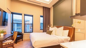 Une chambre d’hôtel équipée d’un lit, d’un bureau, d’une chaise et de grandes fenêtres donnant sur la ville.