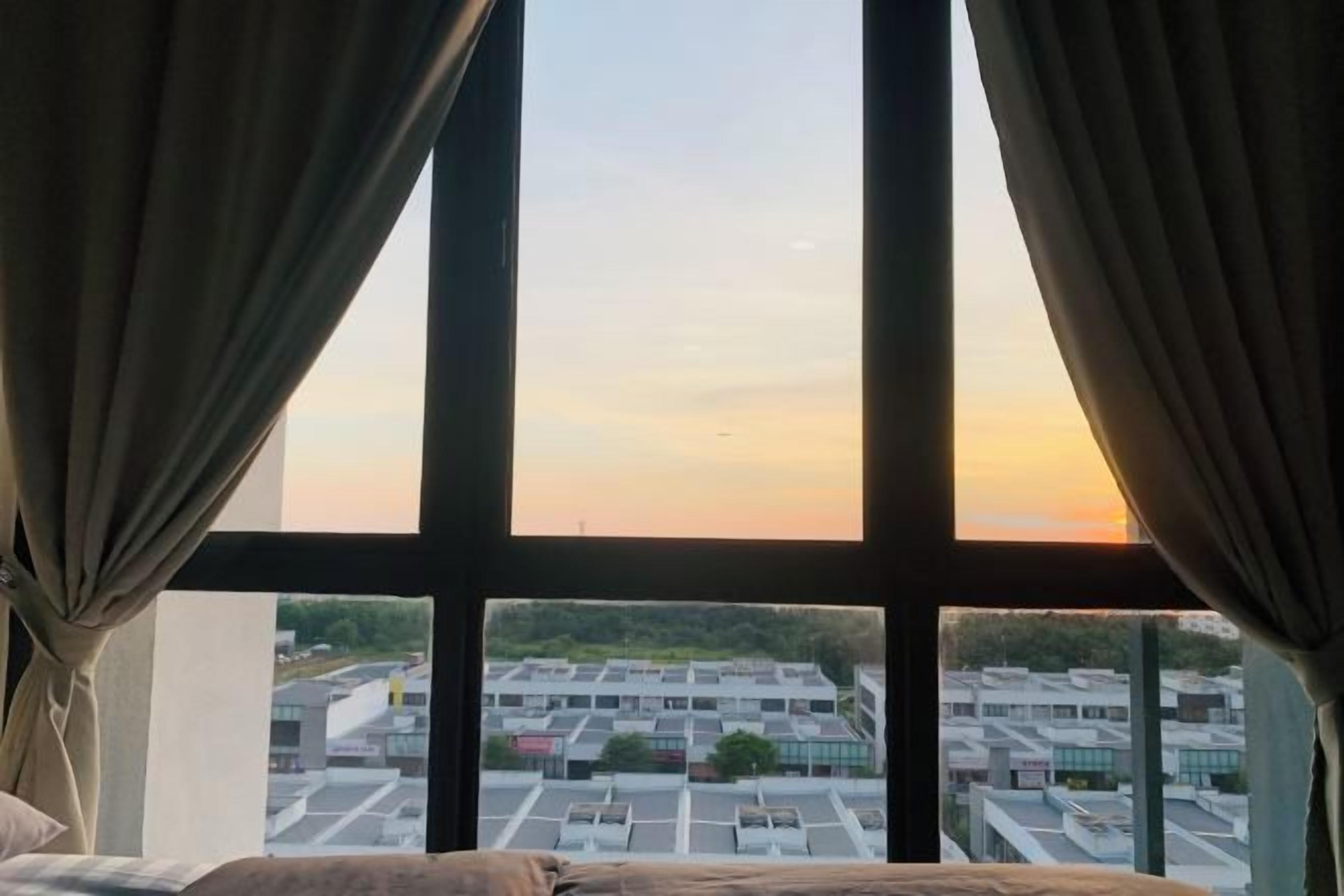 A room with a large window, curtains, and a view of a parking lot and buildings.