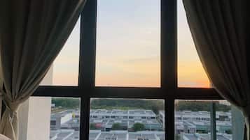 A room with a large window, curtains, and a view of a parking lot and buildings.