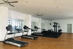 Une salle de sport équipée de tapis de course, d’une machine de musculation et d’un mur entièrement recouvert de miroirs.