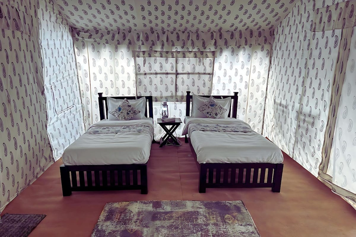 Quarto com duas camas, uma mesinha e cortinas estampadas.