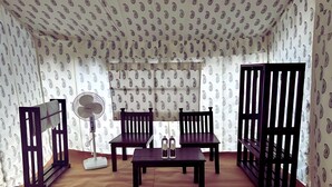 Ein Zimmer mit zwei Holzstühlen, einem Tisch, einem Ventilator und einer Trennwand.