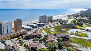 Area costiera urbana con grattacieli, spiaggia e fiume, con vegetazione verde.