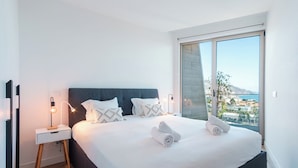 Un dormitorio moderno con una cama grande, dos mesitas de noche y vistas al mar.