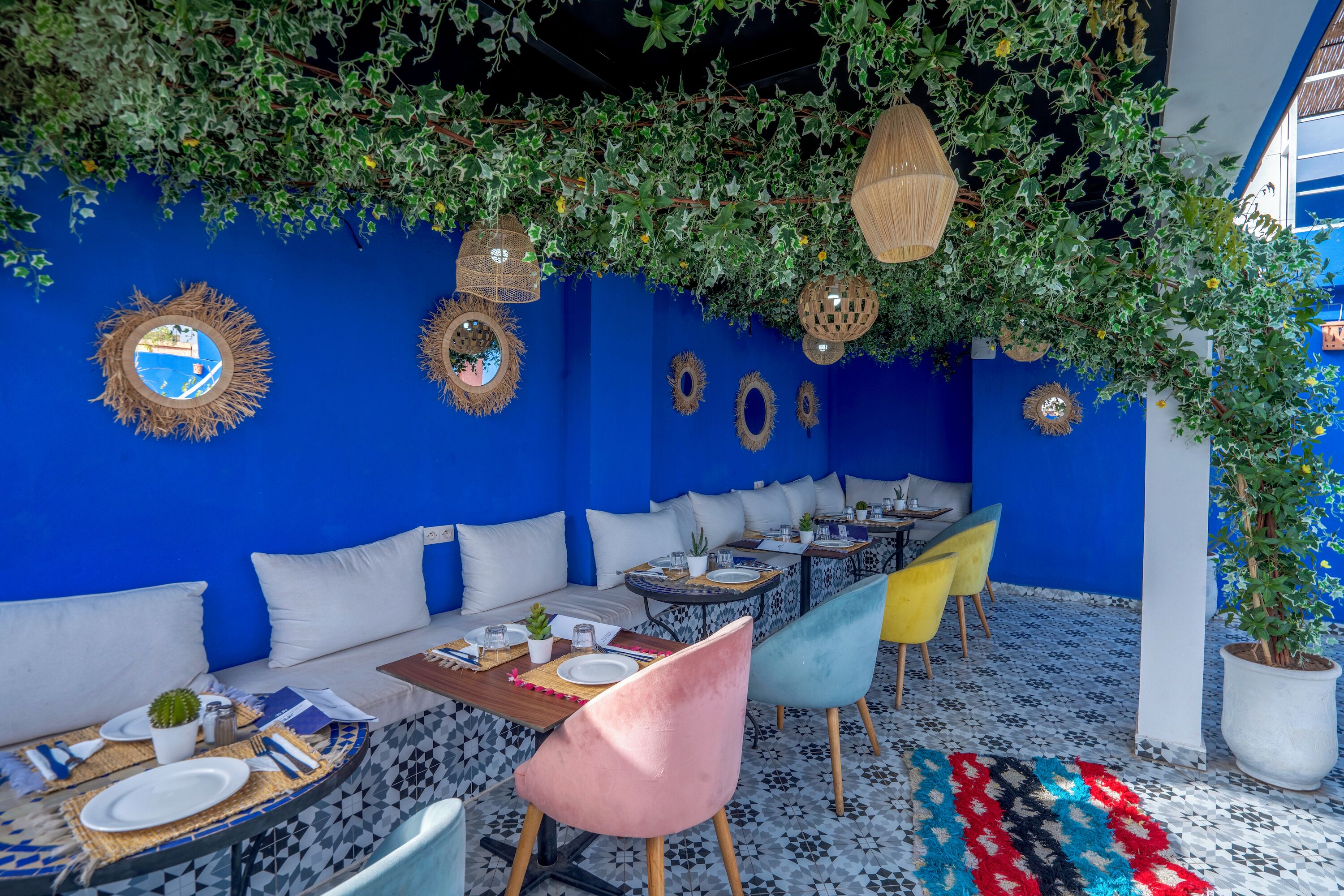 Un restaurante con paredes azules, cojines blancos y sillas coloridas.
