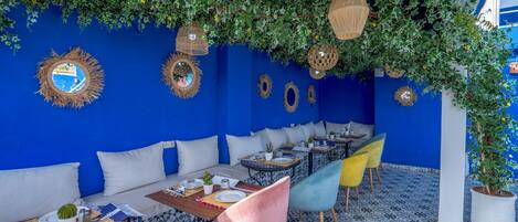 Un restaurante con paredes azules, cojines blancos y sillas coloridas.