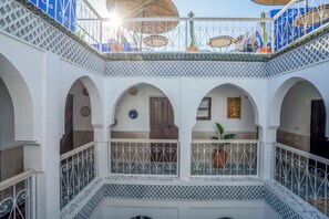 Une cour intérieure à plusieurs niveaux, agrémentée d’arches blanches, d’une rambarde en métal et de plantes en pot.