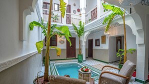 A courtyard with a pool, potted plants, and wicker chairs.