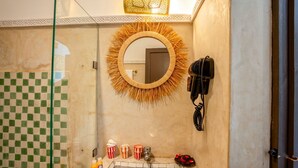 A bathroom with a checkered floor, a round mirror with a straw border, a hairdryer, and a telephone.