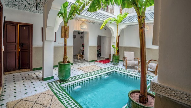 A pool area with tiled flooring, potted plants, and a ceiling with intricate patterns.