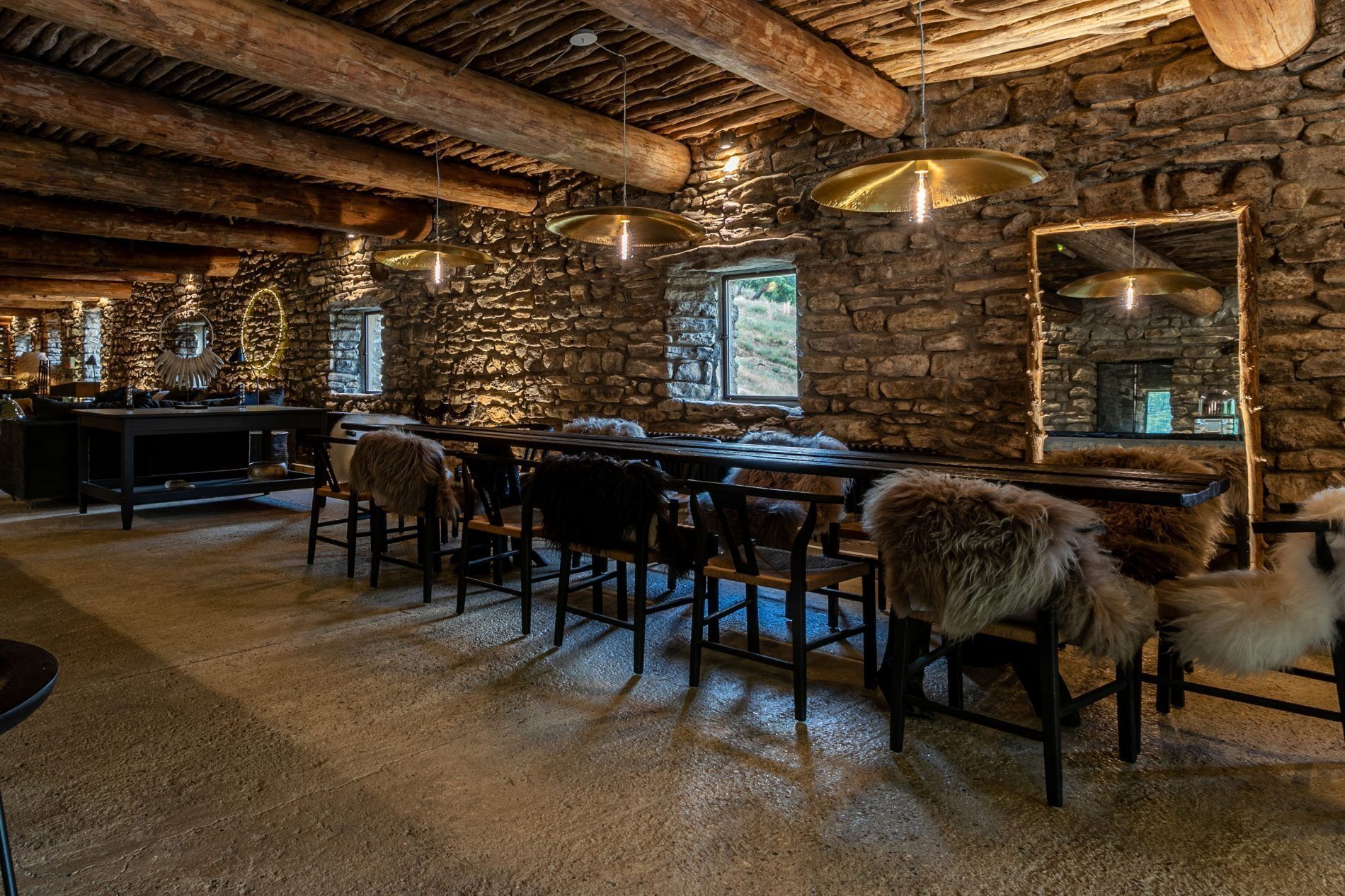 Ein rustikales Interieur mit Steinwänden, Holzbalken und einer Bar mit Sesseln und Felldecken.