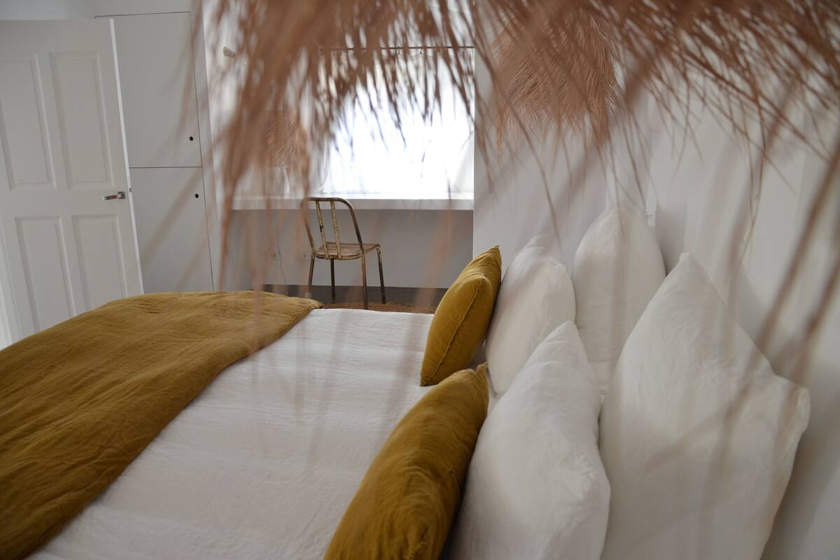Een slaapkamer met een bed, witte muren, een raam en een stoel.