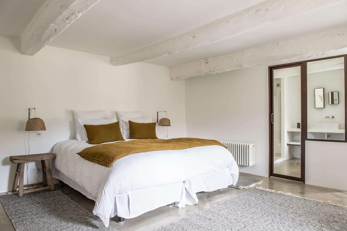 Een slaapkamer met een bed, nachtkastjes, een radiator en een badkamer zichtbaar door een geopende deur.