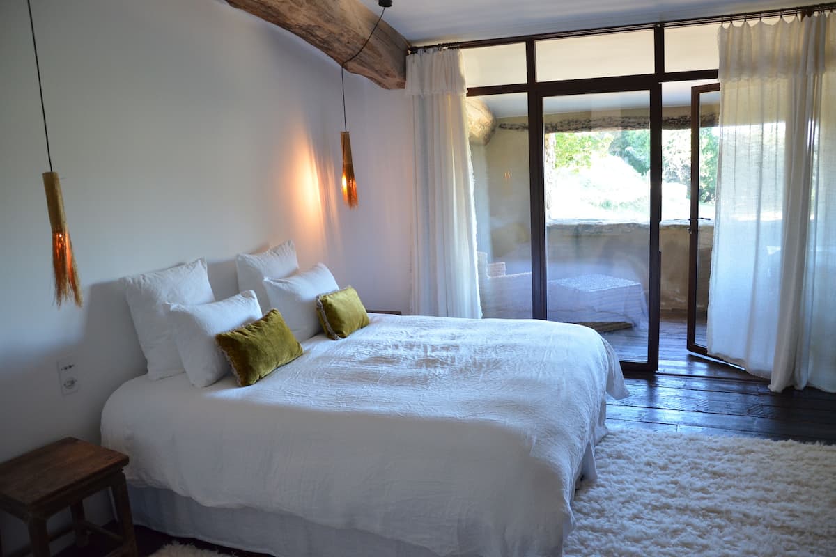 Een slaapkamer met een groot bed, een houten hoofdeinde, een nachtkastje en uitzicht door een glazen deur op een buitenruimte.