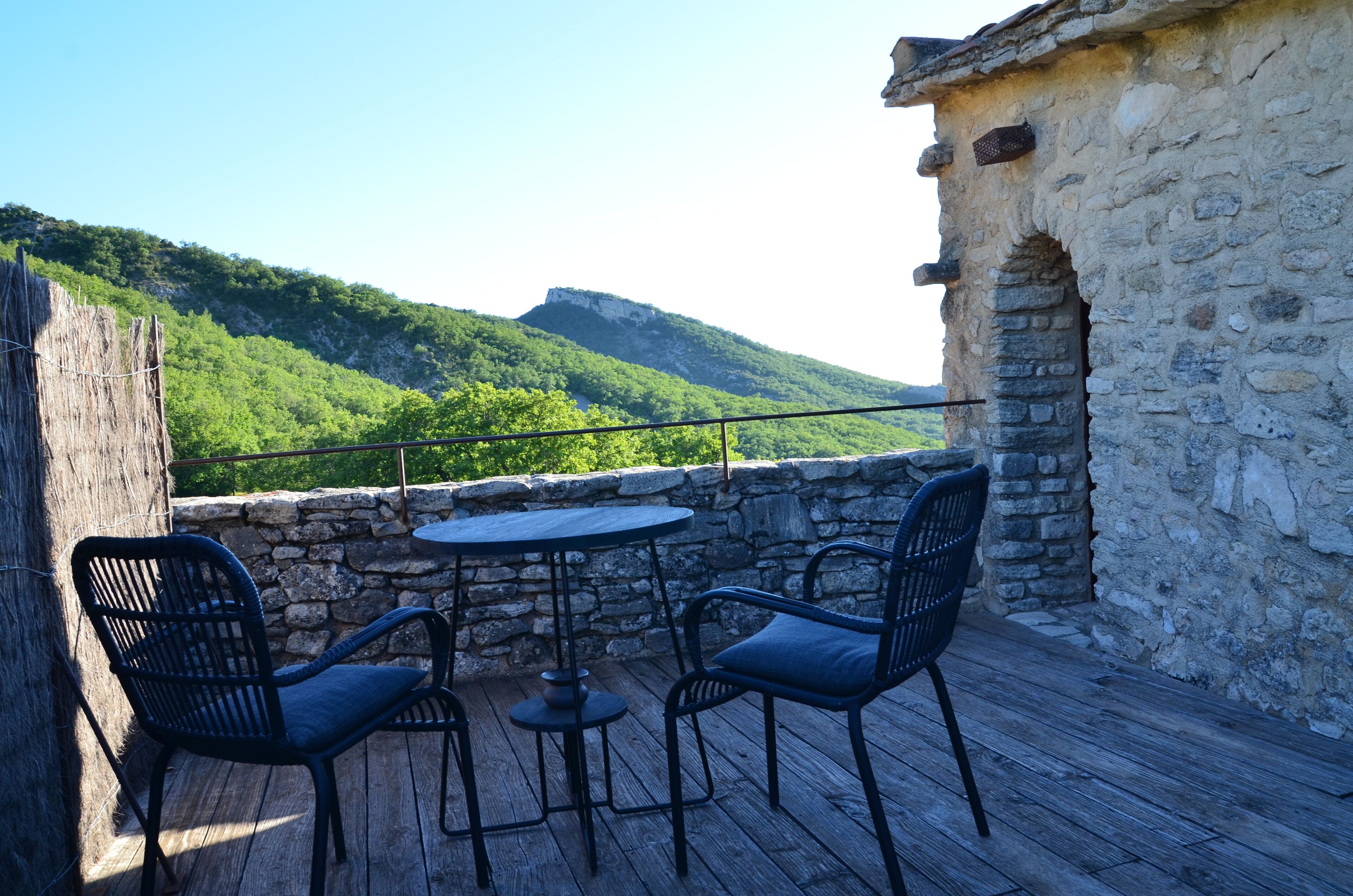 A wooden deck with a stone wall, a round table, and two chairs.