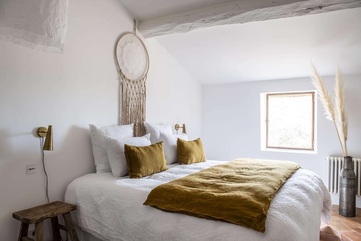 Een slaapkamer met een bed, een macramé wanddecoratie, een raam met pluizige halmen en een radiator.