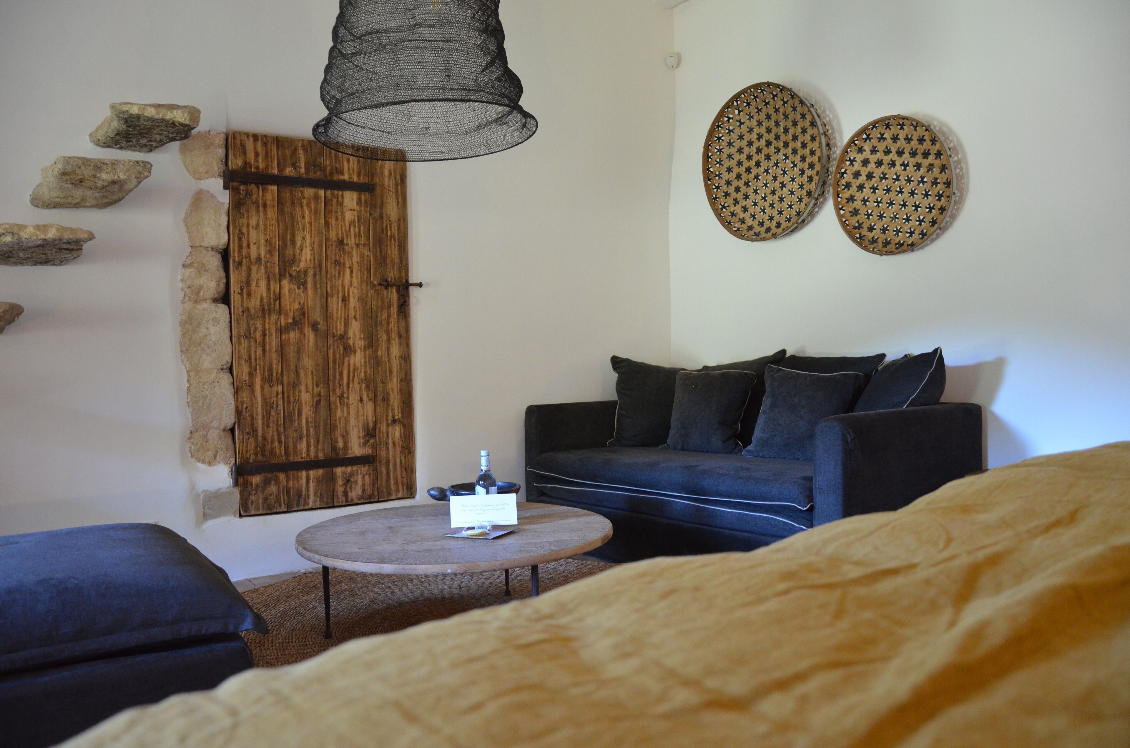 Una stanza accogliente con una porta in legno, un divano nero, un tavolino con una bottiglia e due piastre decorative a parete.