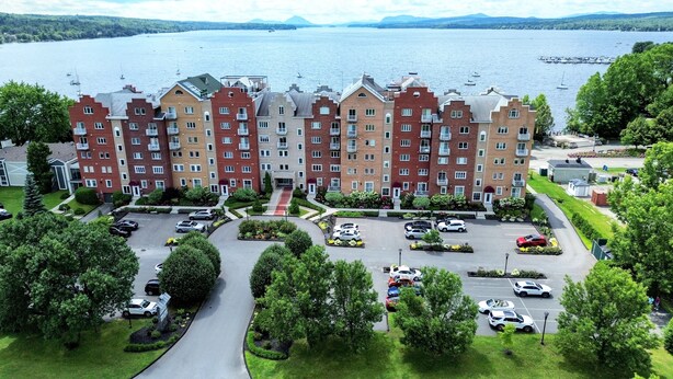 A multi-story residential building with a parking lot in front. - Le Littoral (Magog)