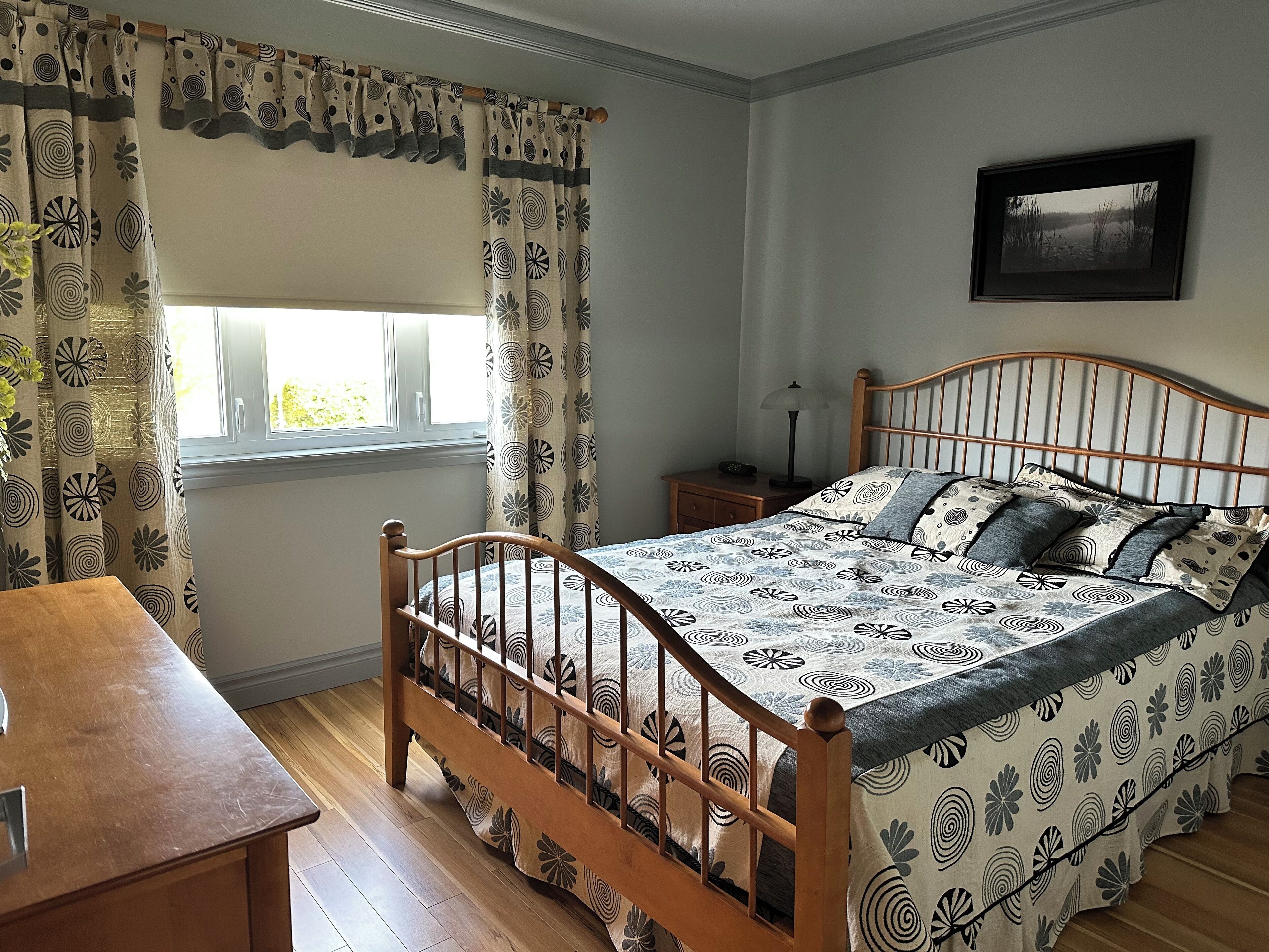 A bedroom with a wooden bed, a nightstand, a desk, and a window with curtains.