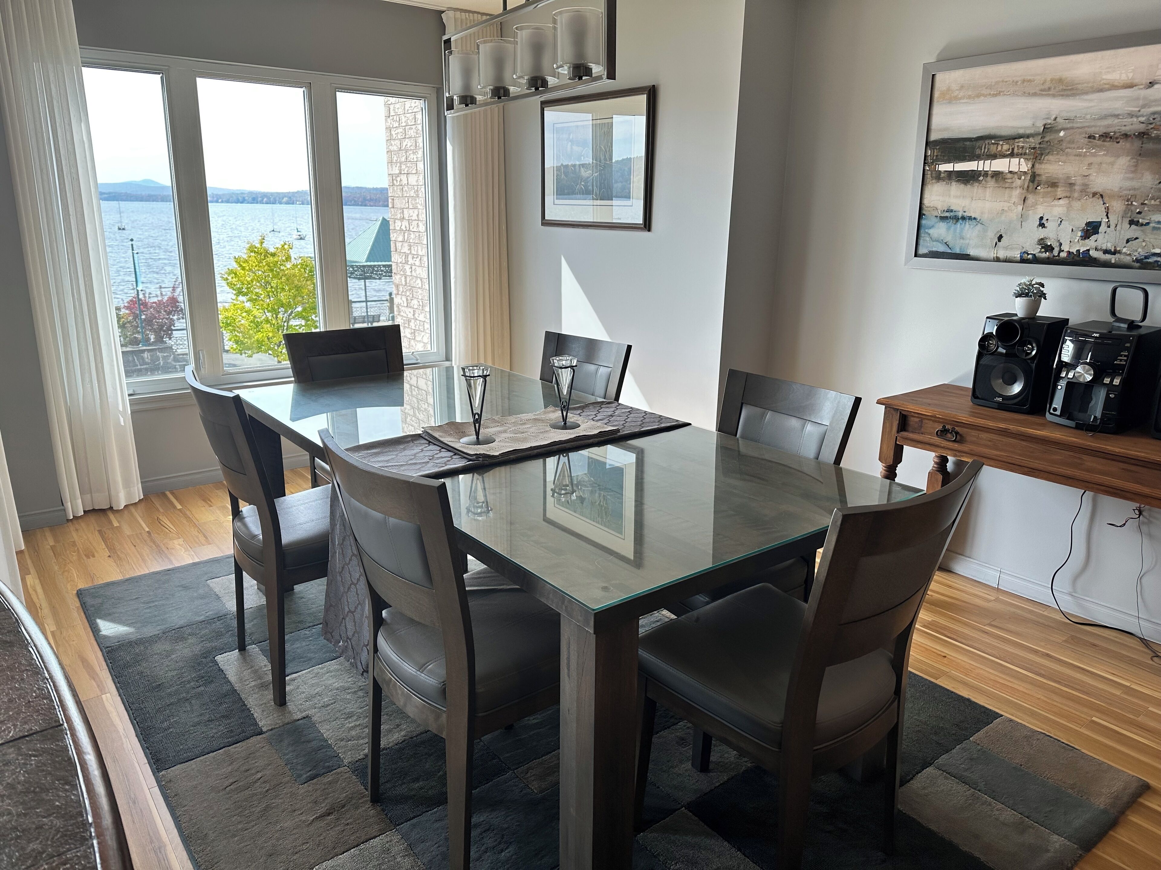 A modern dining room with a glass table, six chairs, and a view of the water.