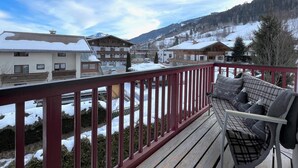 A balcony with a red railing overlooking a snowy village with buildings and mountains in the background. - Kitz Residenz Twelve Kaprun (Kaprun)