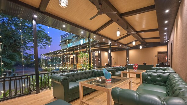 A cozy outdoor seating area with green leather sofas and a glass-top table, surrounded by string lights and wooden flooring. - Khandala Valley Retreat (Mawal)