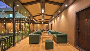 A spacious lounge area with green leather sofas, wooden flooring, and a wooden ceiling with exposed beams. - Khandala Valley Retreat (Mawal)