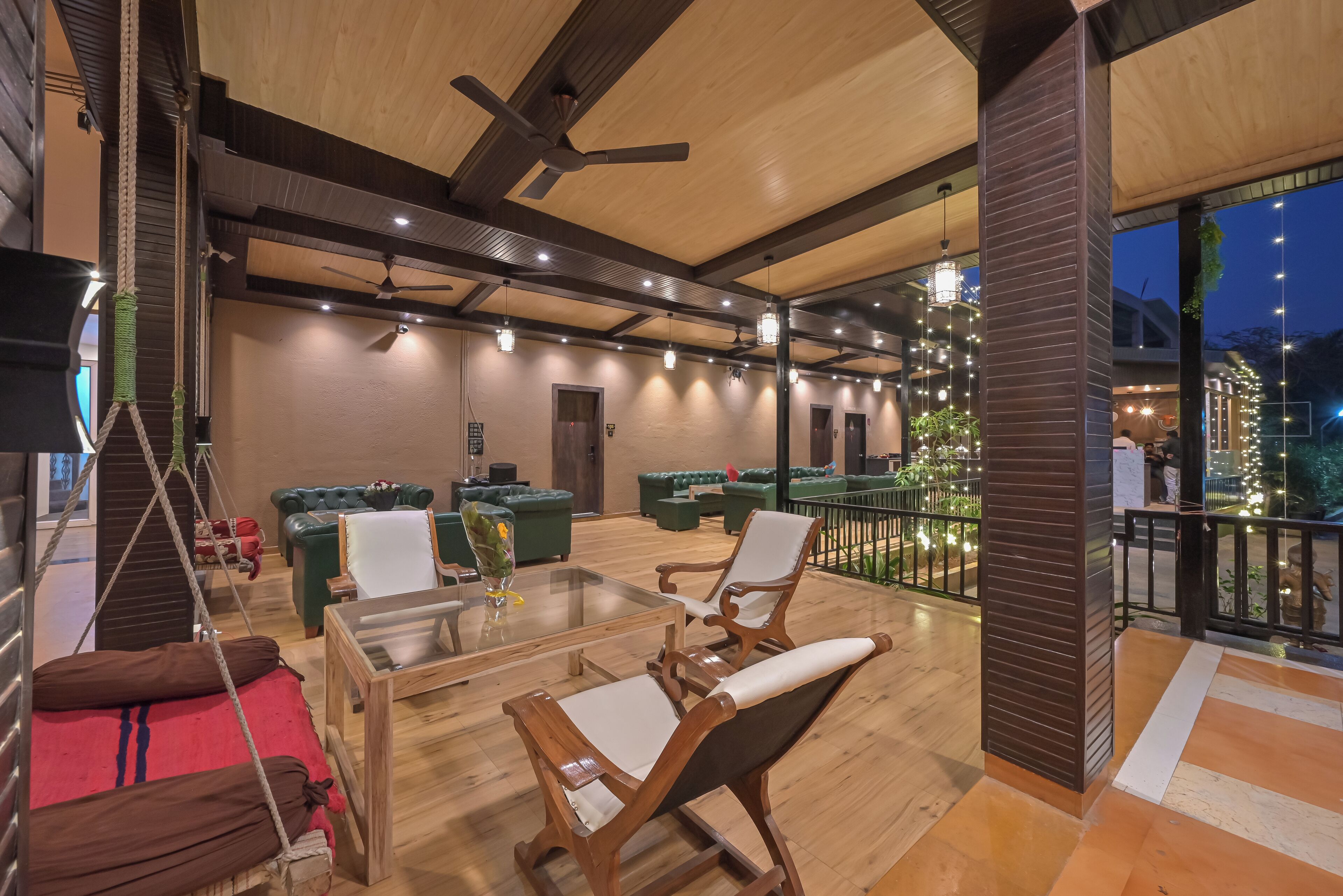 A spacious lounge area with wooden flooring, green sofas, and a glass table.