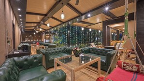 A modern lounge area with green leather sofas, a glass-top coffee table, and a hanging swing. - Khandala Valley Retreat (Mawal)