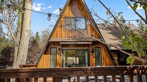 Une cabane en bois avec un toit triangulaire, de grandes fenêtres et une terrasse en bois à l’avant.